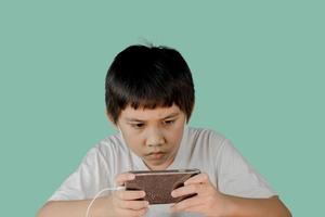 Nahaufnahme des Gesichtes eines Jungen, der Kopfhörer trägt und beabsichtigt, Spiele auf seinem Smartphone zu spielen? foto