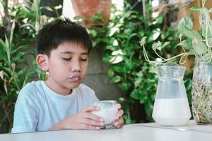 asiatischer Junge in einem weißen T-Shirt trinkt ein Glas Milch foto