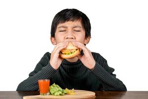 süßer asiatischer Junge im schwarzen Hemd, der einen köstlichen Hamburger isst foto