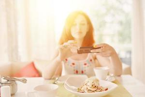 Rothaarige Frau fotografiert Salat mit der Smartphone-Kamera. foto