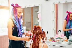 Frau Friseur webt zu Mädchen Ingwer Dreadlocks. foto