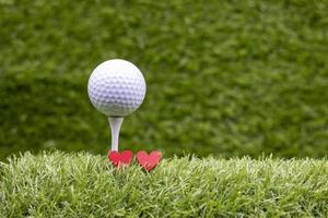 Golfball ist auf Abschlag und zwei rote Herzen auf grünem Gras mit Liebe foto