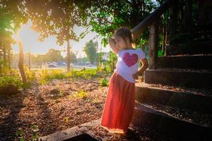 Porträt eines glücklichen asiatischen kleinen Mädchens, das mit Sonnenlicht im Park steht foto