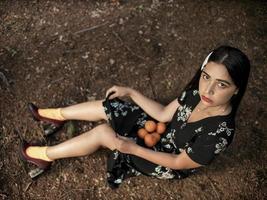 Ein schönes Mädchen mit kaukasischem Aussehen sitzt in einem langen Kleid auf dem Boden und hält viel Mandarine darin. von oben betrachten foto