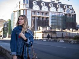 süßes blondes Teen mit wallendem Haar in einer Jeansjacke auf der Brücke im Freien foto