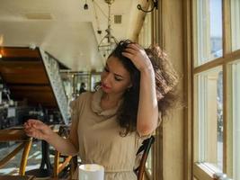 eine lockige Frau sitzt an einem Tisch in einem Café und glättet sich die Haare foto