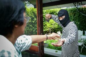männlich Dieb tragen schwarz Maske Tragen groß Messer in das Haus von ein Alten Frau zu rauben und gewaltsam nehmen Weg Vermögen. Versicherung Konzept Schutz von Leben und Eigentum foto