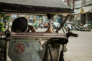 ein Rikscha Abzieher ruhen auf seine Rikscha beim jalan kh zaenal mustafa Tasikmalaya, Indonesien. Tasikmalaya, April 15, 2023 foto