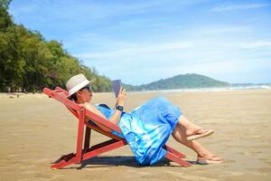 stilvoll Frau tragen ein Blau lange Kleid. sitzen im das Sonnenschein beim das Strand suchen beim das schön natürlich Landschaft. Tourist Meer Strand Thailand, Asien, Sommer- Urlaub Ferien Reise Ausflug foto