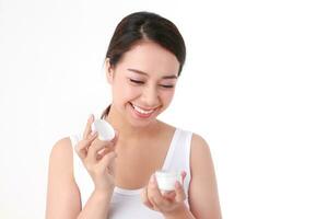 schön asiatisch Frau haben ein schön lächeln, sauber Weiß Zähne. nehmen Pflege von das Gesundheit von Ihre Gesicht mit Haut Cremes. Schönheit Konzept. Weiß Hintergrund foto