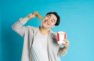 Porträt von asiatisch Mann Essen schnell Essen auf Blau Hintergrund foto