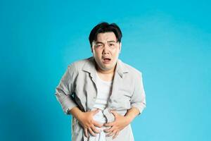 Bild von asiatisch Mann haben Gesundheit Probleme, isoliert auf Blau Hintergrund foto