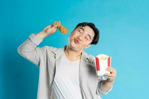 Porträt von asiatisch Mann Essen schnell Essen auf Blau Hintergrund foto