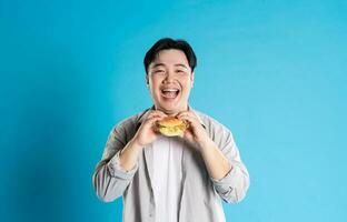 Porträt von asiatisch Mann Essen schnell Essen auf Blau Hintergrund foto
