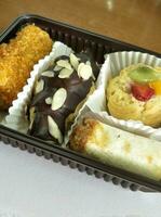 vier Arten von Süss Kuchen und salzig Kuchen sind platziert im ein braun Container gefüttert mit Papier Behälter. foto