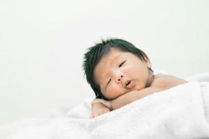 glückliches süßes entzückendes asiatisches Baby mit schwarzem Haar, das eine weiße Decke liegt foto