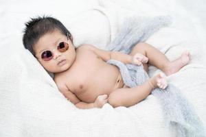 Neugeborenes Baby liegt auf einer weißen Decke. er trägt eine sonnenbrille foto