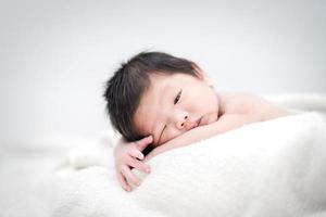 glückliches süßes entzückendes asiatisches Baby mit schwarzem Haar, das auf einem weißen Bett liegt foto