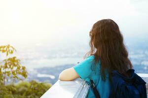 asiatisch jung Frau Blau Kleid tragen Tasche Reisende suchen mit beim bewundern das Aussicht Stadtbild Berg Angebot Hintergrund. foto