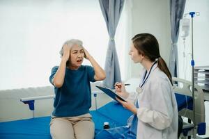 Arzt im Weiß passen nehmen Anmerkungen während diskutieren und asiatisch Alten, Frau geduldig Wer Lügen auf Bett mit Empfang Kochsalzlösung Lösung im Krankenhaus oder Klinik. foto