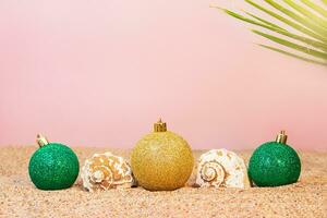 glänzend Gold und Grün Weihnachten Dekorationen mit Muscheln auf Strand auf Sand mit Palme auf sonnig Tag auf Rosa Hintergrund. Platz zum Text. Neu Jahr oder Weihnachten auf das Strand. Urlaub im heiß Länder foto