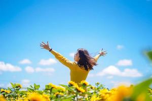 glückliche unbeschwerte Sommerfrau im Sonnenblumenfeld im Frühjahr. fröhliche gemischtrassige asiatische Frau, die mit erhobenen Armen lächelt foto