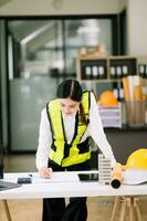 kreativ Architekt Projektion auf das groß Zeichnungen Arbeiten und Laptop mit auf auf architektonisch Projekt beim Konstruktion beim Schreibtisch im Büro. asiatisch Frau Industrie Fachmann foto