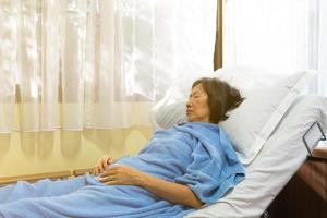 Senior asiatische Frau liegt auf dem Bett neben Fenstern wegen Grippe foto