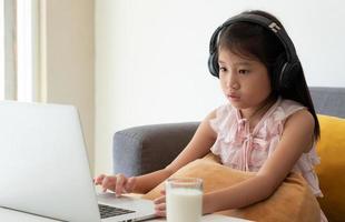 ein junges asiatisches mädchen, das während der covid-19- oder Coronavirus-Pandemie einen Computer verwendet, um zu Hause als Protokoll zur sozialen Distanzierung zu lernen. Homeschooling-Konzept foto