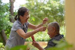 ältere asiatische frau, die ihrem mann auf der terrasse haarschnitt foto