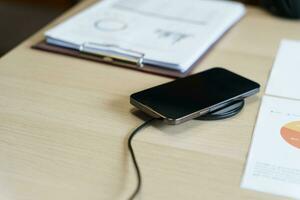 Laden Handy, Mobiltelefon Telefon Batterie mit kabellos Laden Gerät im das Tisch. Smartphone Laden auf ein Laden Pad. Handy, Mobiltelefon Telefon in der Nähe von kabellos Ladegerät modern Lebensstil Technologie Konzept foto