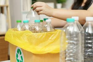 Zuhause recyceln Öko Grün Null Konzept Frau werfen leeren Plastik Flasche im Recycling Behälter mit Gelb Müll Taschen beim heim. foto