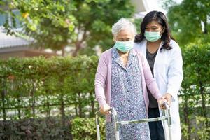 Arzt hilft asiatischen Senioren oder älteren alten Damen, die mit Gehhilfe gehen und eine Gesichtsmaske tragen, um die Sicherheitsinfektion zu schützen und das neuartige Coronavirus Covid-19-Virus abzutöten.