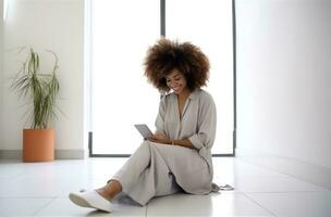 weiblich afro Haar Stylist Frau Sitzung auf Fußboden suchen beim Smartphone foto