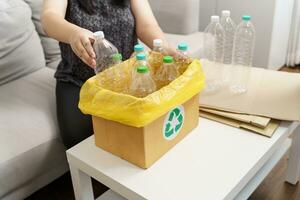 Zuhause recyceln Öko Grün Null Konzept Frau werfen leeren Plastik Flasche im Recycling Behälter mit Gelb Müll Taschen beim heim. foto