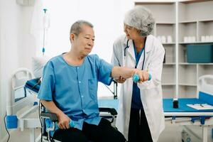 asiatisch Physiotherapeut Portion Alten Mann geduldig Dehnen Arm während Übung richtig mit Hantel im Hand während Ausbildung Hand im Bett im Klinik foto