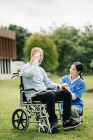 Alten asiatisch Senior Mann auf Rollstuhl mit asiatisch Vorsichtig Betreuer. Pflege- Zuhause Krankenhaus Garten Konzept sind Gehen im das Garten. zu Hilfe und ermutigen. foto