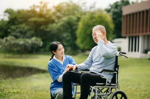 Alten asiatisch Senior Mann auf Rollstuhl mit asiatisch Vorsichtig Betreuer. Pflege- Zuhause Krankenhaus Garten Konzept sind Gehen im das Garten. zu Hilfe und ermutigen. foto