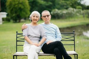 asiatisch Senior Paar haben ein gut Zeit. Sie Lachen und lächelnd während Sitzung draussen beim das Park. schön Senior Paar foto