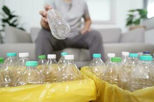 Zuhause recyceln Öko Grün Null Konzept Mann werfen leeren Plastik Flasche im Recycling Behälter mit Gelb Müll Taschen beim Zuhause foto