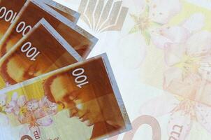 100 israelische neue Schekel-Scheine liegen im Stapel auf dem Hintergrund einer großen halbtransparenten Banknote. abstrakter betriebswirtschaftlicher hintergrund foto