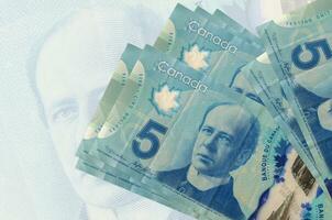 5 kanadische Dollarscheine liegen im Stapel auf dem Hintergrund einer großen halbtransparenten Banknote. abstrakte Darstellung der Landeswährung foto