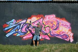 jung kaukasisch männlich Graffiti Künstler Zeichnung groß Straße Kunst Gemälde im Blau und Rosa Töne foto