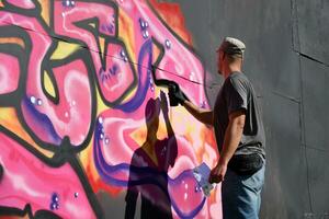 jung kaukasisch männlich Graffiti Künstler Zeichnung groß Straße Kunst Gemälde im Blau und Rosa Töne foto