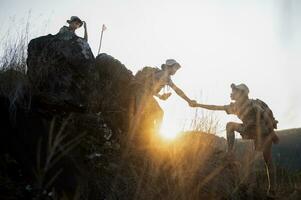 Junge Pfadfinder Mannschaft Klettern mit Rucksäcke Stehen auf Berg Junge Pfadfinder jubeln beim Felsen Klettern Erfolg im erkunden Lager beim Sonnenuntergang. erkunden Lager Sicht. foto