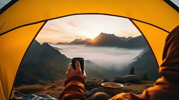 Camping halten ein Tasse im ein öffnen Gelb Zelt mit ein neblig Berg zündete durch natürlich Licht. foto