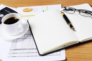 Geschäftskonzept mit leeren Buchseiten und Glas- und Kaffeetasse und Taschenrechner mit Dokument auf dem Arbeitstisch foto