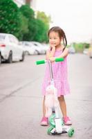 Porträt eines kleinen asiatischen Mädchens mit Roller und Puppe auf der Straße foto