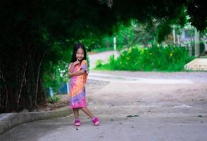 Porträt eines glücklichen asiatischen kleinen Mädchens im Kleid, das auf einem Fußweg im Park steht foto