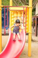 asiatisches kleines Mädchen spielt gerne Slider auf einem Kinderspielplatz foto